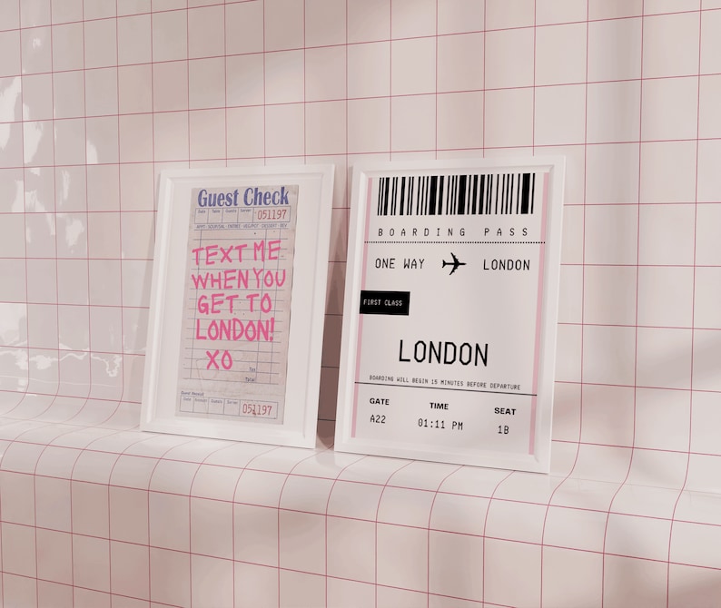 May include: Two framed prints on a white tiled wall. The left print is a white frame with a pink and white guest check that says "Text me when you get to London! XO". The right print is a white frame with a black and white boarding pass that says "Boarding Pass One Way London First Class London Gate A22 Time 01:11 PM Seat 18".