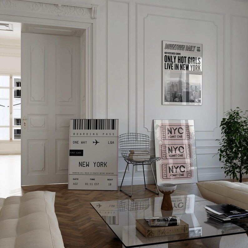 Pode incluir: Um interior de sala de estar com uma parede branca e uma mesa de caf&eacute; de vidro. H&aacute; dois cartazes na parede, um com o texto "Downtown Daily" e o texto "Only Hot Girls Live in New York" e o outro com o texto "NYC Admit One". H&aacute; uma cadeira com uma estrutura de metal e um sof&aacute; branco na sala.