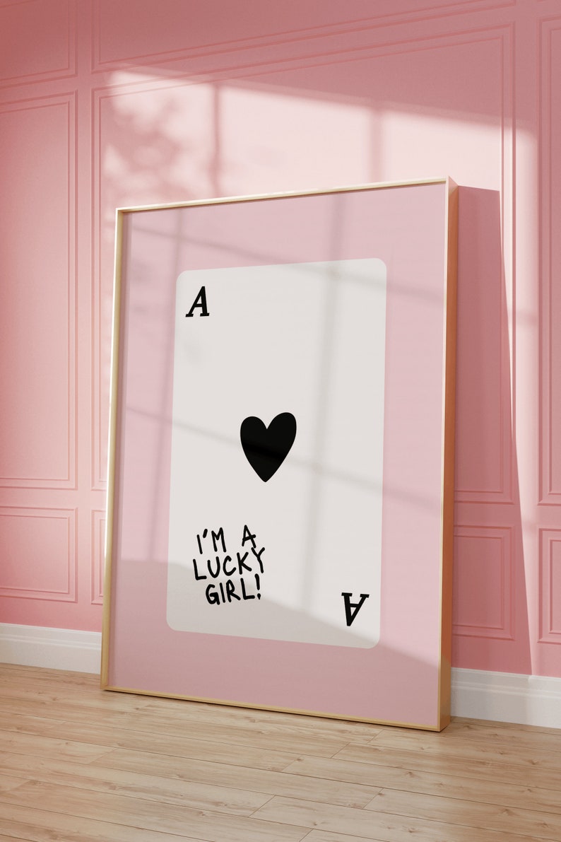 Puede incluir: Una impresi&oacute;n enmarcada de una carta de juego con un coraz&oacute;n negro y el texto "I'm a lucky girl!" sobre un fondo rosa.