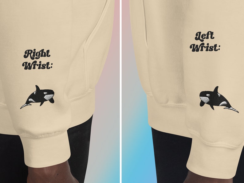 May include: A beige sweatshirt with black embroidered orcas on the sleeves. The left sleeve has the text "Left Wrist:" and the right sleeve has the text "Right Wrist:".