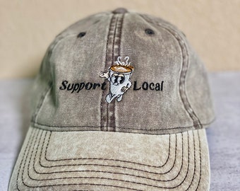 May include: A brown and beige baseball cap with an embroidered design of a coffee cup with steam and the text "Support Local".