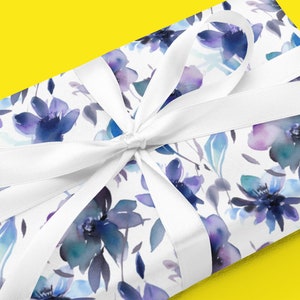 May include: A white gift box wrapped in blue and purple watercolor floral patterned paper with a white satin ribbon tied in a bow.