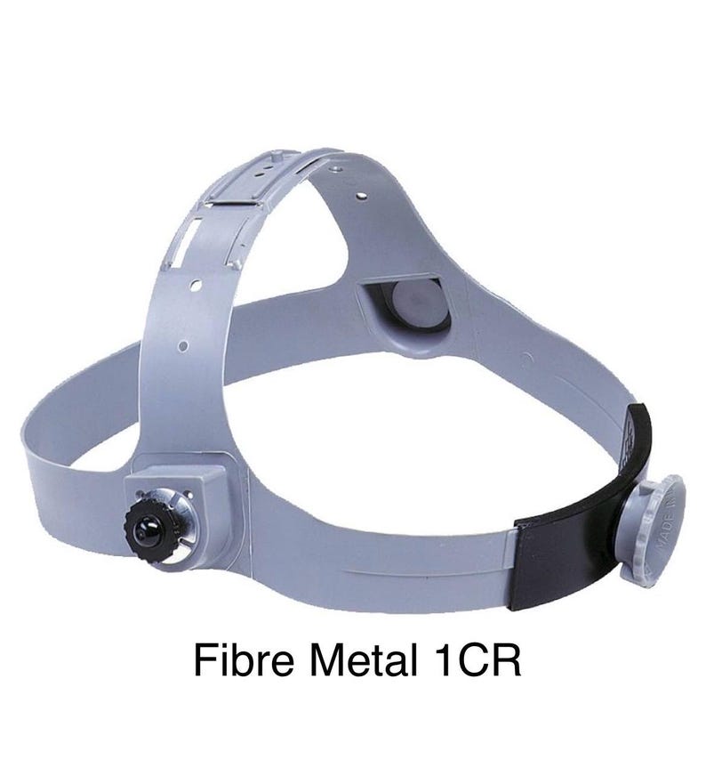 May include: A gray Fibre Metal 1CR welding helmet headgear. The headgear has a black adjustment knob, a black leatherette band, and a gray plastic frame. The text "Fibre Metal 1CR" is printed in black at the bottom of the image.