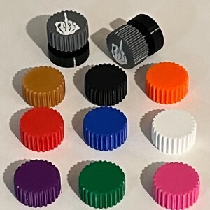 May include: A collection of colorful, ribbed bottle caps. Two caps feature a gray and black design with a white hand gesture. Other caps are in various colors, including gold, black, orange, red, blue, white, purple, green, and pink.