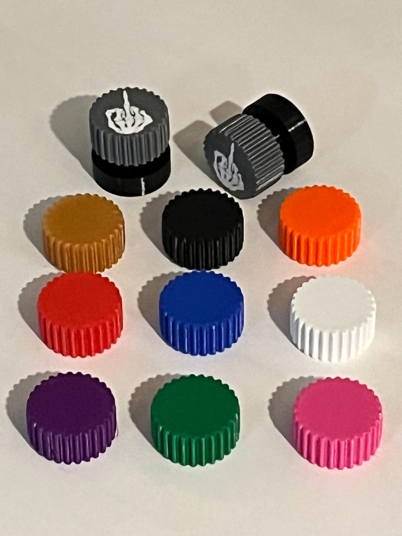 May include: A collection of colorful, ribbed bottle caps. Two caps feature a gray and black design with a white hand gesture. Other caps are in various colors, including gold, black, orange, red, blue, white, purple, green, and pink.