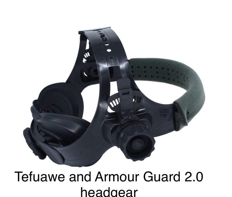 May include: Black welding headgear with a green padded head support. The headgear has adjustable straps and a large lens area. The text "Tefuawe and Armour Guard 2.0 headgear" is printed at the bottom of the image.