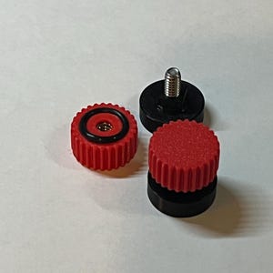 Puede incluir: Tres peque&ntilde;os componentes mec&aacute;nicos. Dos son rojos con un borde estriado y un anillo negro. Uno tiene un tornillo plateado. El otro componente es negro con un tornillo plateado. Los componentes son para un dispositivo mec&aacute;nico.