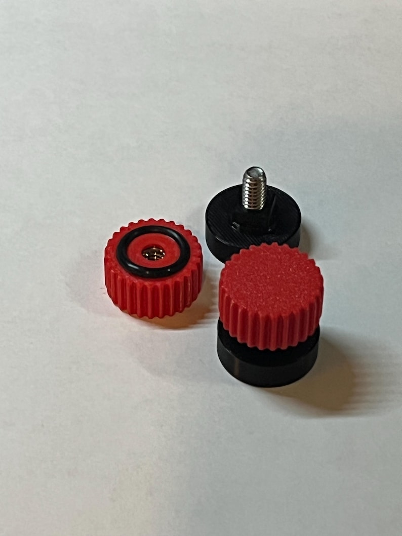 Puede incluir: Tres peque&ntilde;os componentes mec&aacute;nicos. Dos son rojos con un borde estriado y un anillo negro. Uno tiene un tornillo plateado. El otro componente es negro con un tornillo plateado. Los componentes son para un dispositivo mec&aacute;nico.