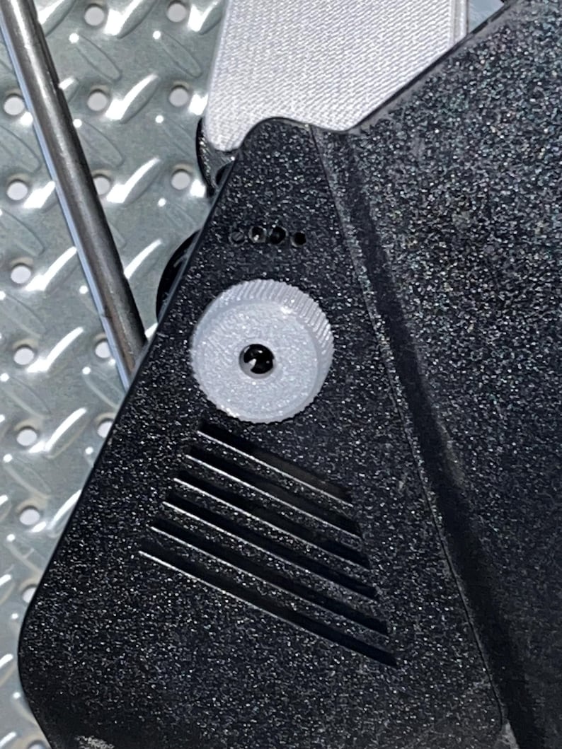 May include: Close-up of a black plastic object with a white knob and a series of vertical lines. The object has a textured surface.