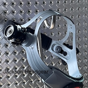 May include: A Jackson Headgear product, a gray and black headgear with a red accent. The headgear has a curved design with adjustable straps and a black padded area for comfort. The text "Jackson Headgear" is visible.