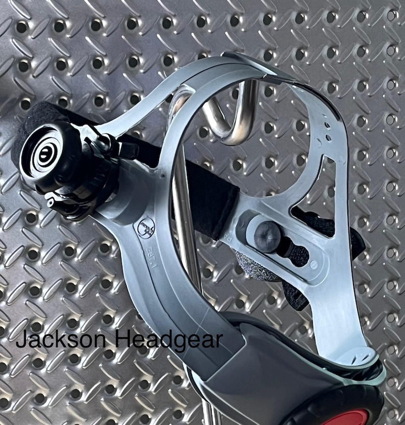 May include: A Jackson Headgear product, a gray and black headgear with a red accent. The headgear has a curved design with adjustable straps and a black padded area for comfort. The text "Jackson Headgear" is visible.