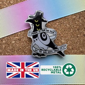 May include: A metal pin badge with a cartoon bird design, wearing a hat. The badge has the text "I MADE IT FOR THE TIGER...BUT THE BIRD KEEPS TAKING IT!" The background is a corkboard with a rainbow ribbon. Made in the UK.
