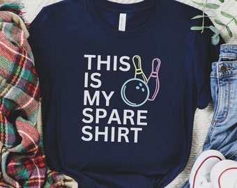 Może przedstawiać: Granatowa koszulka z napisem "THIS IS MY SPARE SHIRT" i grafiką z kulą i kręglami do kręgli. Koszulka jest połączona z jasnymi dżinsami, białymi trampkami i szalikiem w kratę. Swobodny strój.