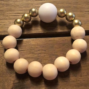 May include: A wooden bead bracelet with a large white bead in the center and gold beads on either side.