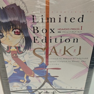 Puede incluir: Una caja "Edici&oacute;n Limitada" SAKI. La caja roja y negra est&aacute; envuelta en pl&aacute;stico transparente. La parte delantera presenta una ilustraci&oacute;n de anime de un personaje con gafas y el texto "HEAVEN'S PRISON 1".