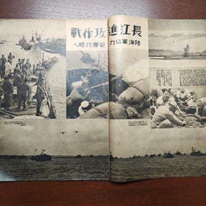 May include: A vintage Japanese newspaper spread featuring black and white photographs of military scenes. The images depict soldiers, ships, and aircraft, with Japanese text headlines and captions. The paper has a sepia tone.