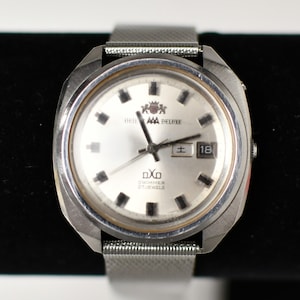 May include: A silver-toned Orient AAA Deluxe watch with a mesh band. The watch face is silver with black markers and hands. The date is displayed as "18" in a small window. The watch also has the text "DXO SWIMMER 27 JEWELS".