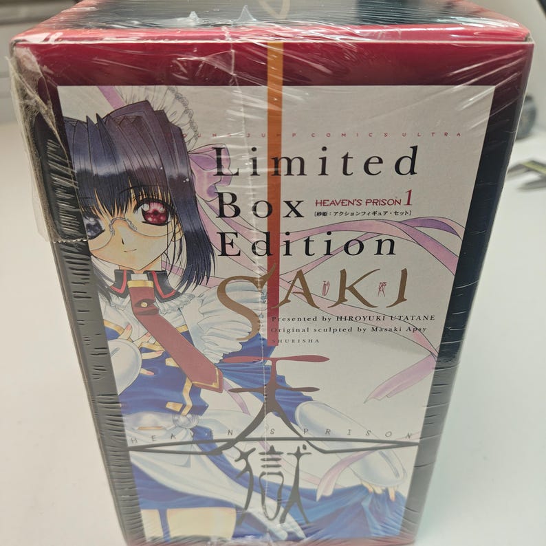 Puede incluir: Una caja "Edici&oacute;n Limitada" SAKI. La caja roja y negra est&aacute; envuelta en pl&aacute;stico transparente. La parte delantera presenta una ilustraci&oacute;n de anime de un personaje con gafas y el texto "HEAVEN'S PRISON 1".