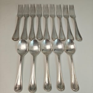 May include: A set of thirteen silver-toned metal utensils consisting of eight four-tined forks and five spoons. Each piece features a smooth, rounded handle with a subtle beaded border detail along the edges and a polished, reflective finish.