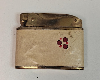May include: Vintage lighter with a cream-colored body and gold-toned metal accents. The lighter features a red floral design on the front. The lighter is rectangular in shape.