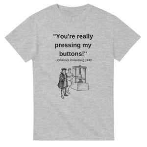Puede incluir: Una camiseta gris con una ilustración en blanco y negro de una prensa de impresión y dos personas. El texto en la camiseta dice "You're really pressing my buttons!" - Johannes Gutenberg 1440.