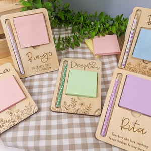 May include: Set of five personalized wooden notepads with a pencil holder. Each notepad has a different name and a floral design. The notepads are pink, light blue, green, purple, and white. The text on the notepads reads "Veena", "Bingo", "Deepthi", "Bella", and "Rita".