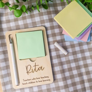 May include: A wooden notepad holder with a green sticky note, a pen, and the name "Rita" engraved on it. The text "Teachers who love teaching, teach children to love learning." is also engraved on the holder.
