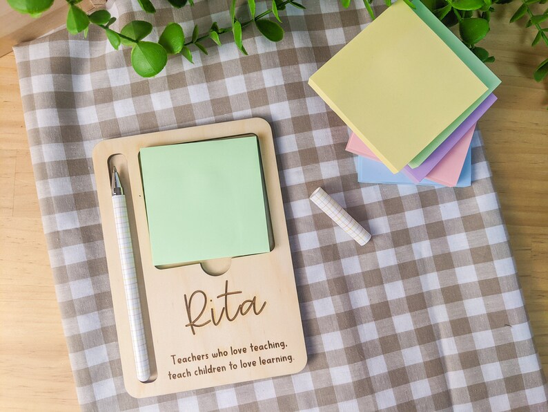 May include: A wooden notepad holder with a green sticky note, a pen, and the name "Rita" engraved on it. The text "Teachers who love teaching, teach children to love learning." is also engraved on the holder.