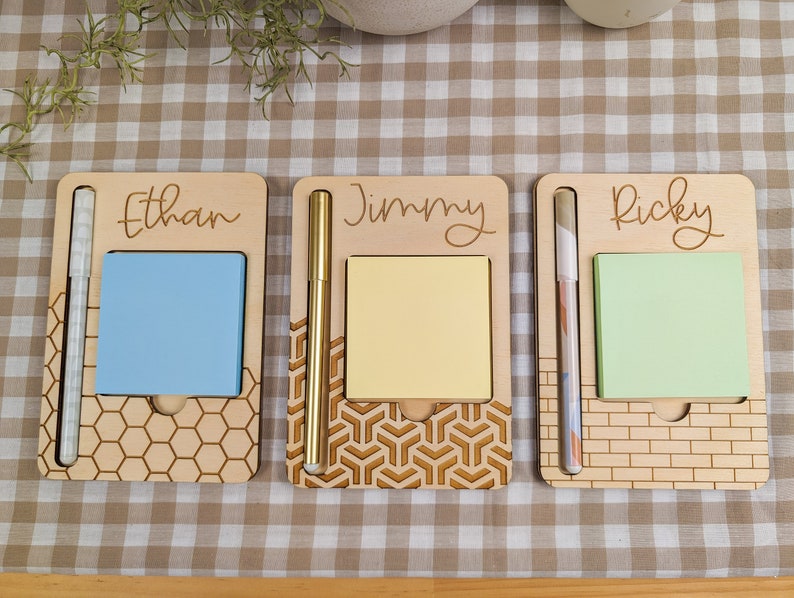 May include: Three wooden note holders with personalized names "Ethan", "Jimmy", and "Ricky". Each holder has a pen slot, a space for sticky notes, and a different laser-cut design.