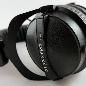 Puede incluir: Auriculares negros de diadema con una diadema negra y una etiqueta plateada que dice "DT 770 PRO 32 OHM".
