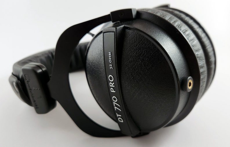 Puede incluir: Auriculares negros de diadema con una diadema negra y una etiqueta plateada que dice "DT 770 PRO 32 OHM".