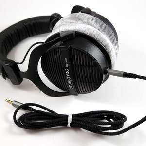 Puede incluir: Auriculares negros de diadema con una almohadilla gris y un cable trenzado negro. Los auriculares tienen el texto "DT 990 PRO 32 Ohm" impreso en el lateral.