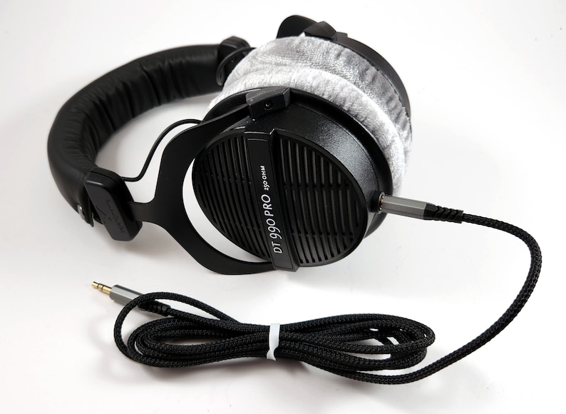 Puede incluir: Auriculares negros de diadema con una almohadilla gris y un cable trenzado negro. Los auriculares tienen el texto "DT 990 PRO 32 Ohm" impreso en el lateral.