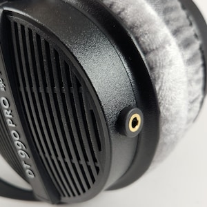 Puede incluir: Auriculares negros con una almohadilla gris y el texto "DT 990 PRO 250 OHM" en el lateral. Los auriculares tienen un conector de audio dorado.