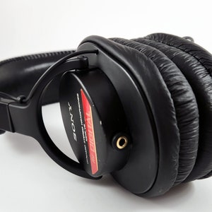 Puede incluir: Auriculares negros de diadema con una etiqueta roja y blanca que dice "Digital Audio" y "Sony" en blanco. Los auriculares tienen una diadema gruesa y acolchada y almohadillas para los o&iacute;dos.