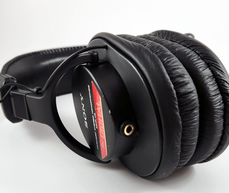 Puede incluir: Auriculares negros de diadema con una etiqueta roja y blanca que dice "Digital Audio" y "Sony" en blanco. Los auriculares tienen una diadema gruesa y acolchada y almohadillas para los o&iacute;dos.