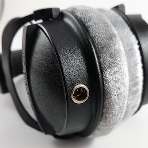 Puede incluir: Primer plano de un auricular negro con una almohadilla de terciopelo gris y un conector de 3,5 mm plateado.
