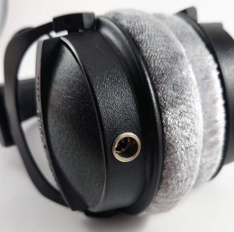 Puede incluir: Primer plano de un auricular negro con una almohadilla de terciopelo gris y un conector de 3,5 mm plateado.