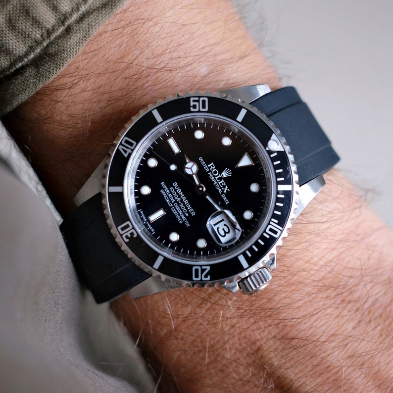 Pu&ograve; includere: Un orologio Rolex Submariner nero con una lunetta argentata e un cinturino in gomma nero. Il quadrante dell'orologio ha una finestrella per la data alle 3 e il testo "Rolex Oyster Perpetual Date Submariner 1000m-300m Superlative Chronometer Officially Certified" &egrave; stampato sul quadrante.