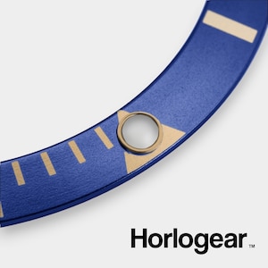 May include: A blue watch bezel with gold accents and a circular hole in the center. The bezel is made of metal and has a textured surface.