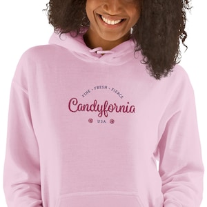 May include: Pink hoodie with a graphic design that says "Candyfornia" in a pink script font with the words "Fine, Fresh, Fierce" in a blue font above the word "Candyfornia" and "USA" in a blue font below the word "Candyfornia".
