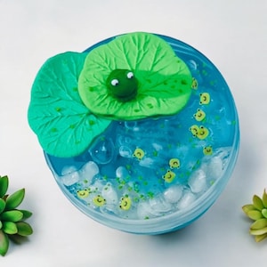 May include: A blue slime with white and green glitter, a green frog on a green lily pad, and white and green frog charms.