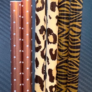 Könnte beinhalten: Eine Auswahl an dekorativen Papierstrohhalmen. Zwei Strohhalme sind kupferfarben mit weißen Punkten. Zwei haben einen Leoparden-Print und zwei ein Tigerstreifen-Design. Für Getränke.