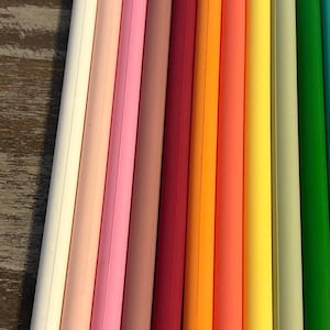 Può includere: Primo piano di una collezione di oggetti cilindrici colorati. I colori includono bianco, rosa, rosso, arancione, giallo e verde. Gli oggetti sono disposti verticalmente, uno accanto all'altro.