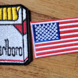 May include: Two embroidered patches, one with a red, white, and blue American flag and the other with a white pack of cigarettes with the word "Marlboro" printed on it.