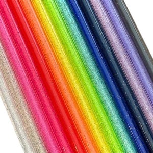 Op de afbeelding: Een diagonale opstelling van glinsterende, cilindrische objecten in regenboogkleuren. De kleuren zijn zilver, roze, rood, oranje, geel, groen, blauw, paars en zwart. De objecten zijn in een spectrum gerangschikt.