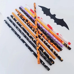 May include: A collection of Halloween-themed straws in various colors, including black, orange, and white, decorated with spiderwebs, bats, and jack-o'-lanterns. A black bat-shaped cutout is also present, perfect for a spooky celebration.