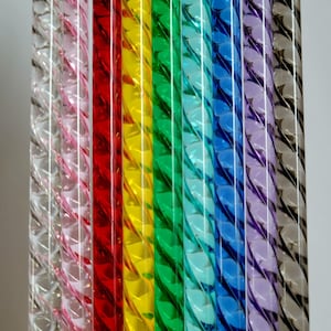 Op de afbeelding: Zeven glazen staven met een spiraalvormig ontwerp. De staven zijn helder, roze, rood, geel, groen, blauw en paars.