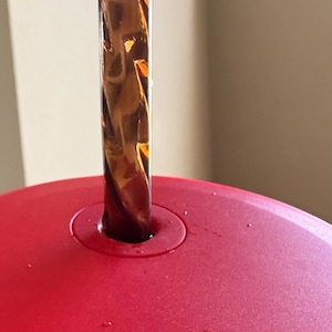 May include: A red lid with a clear, brown, swirl-patterned straw inserted into the lid. The lid has the word "WS" printed on it.