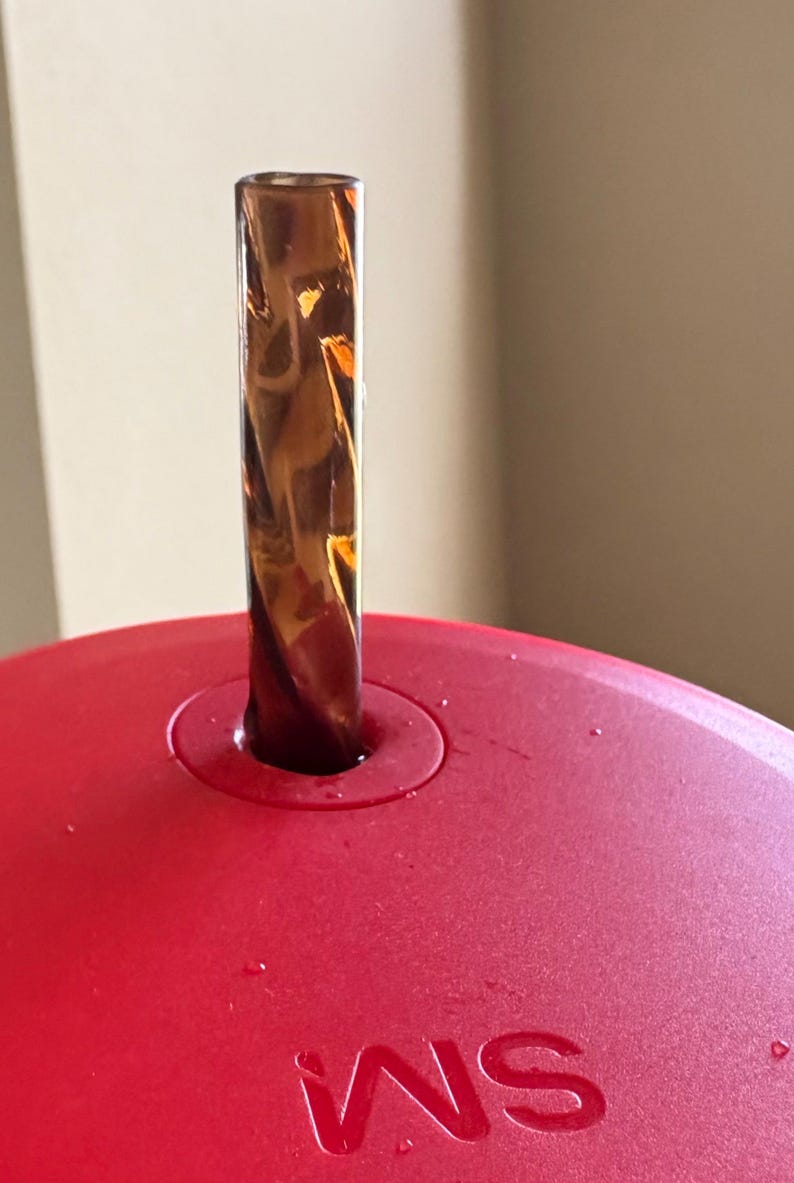 May include: A red lid with a clear, brown, swirl-patterned straw inserted into the lid. The lid has the word "WS" printed on it.